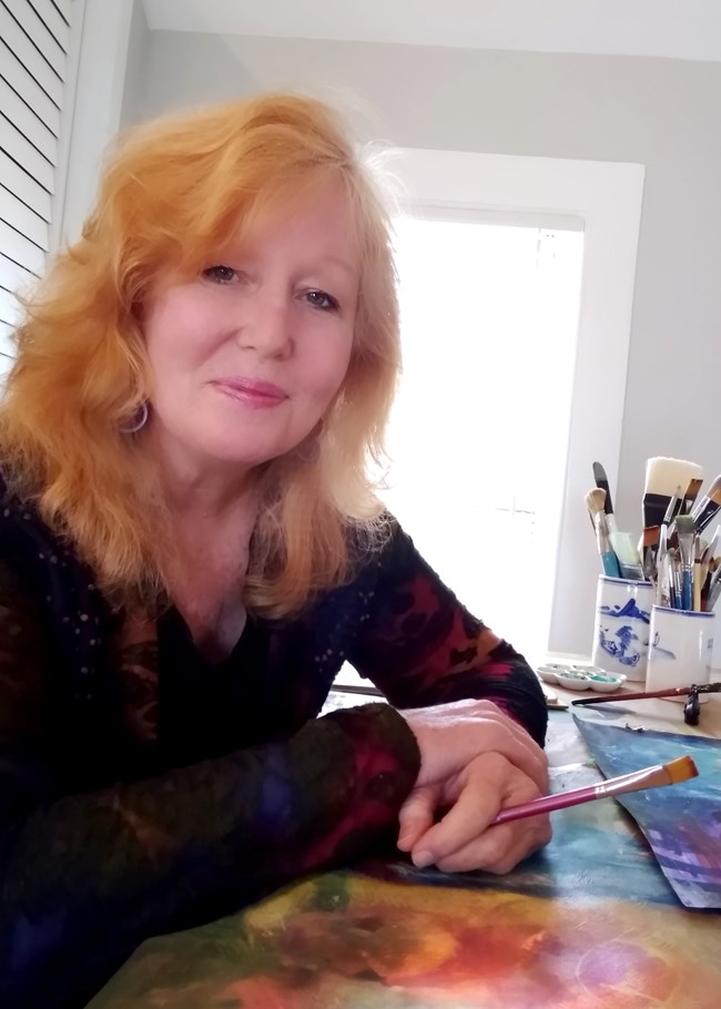 Photo portrait of smiling woman with red hair holding a fine art paint brush