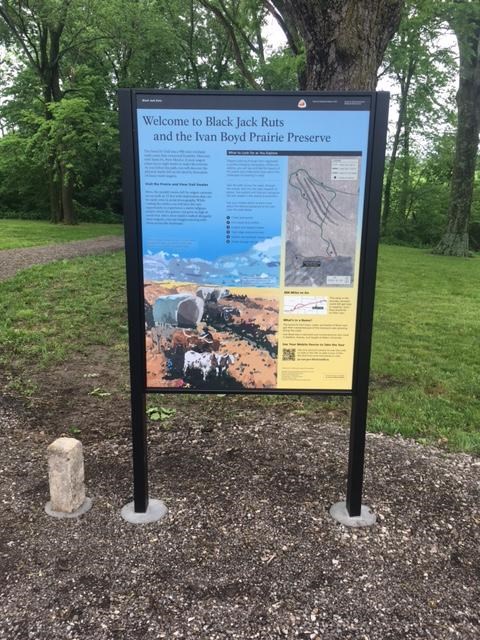 An upright wayside exhibit sitting on a stone path.