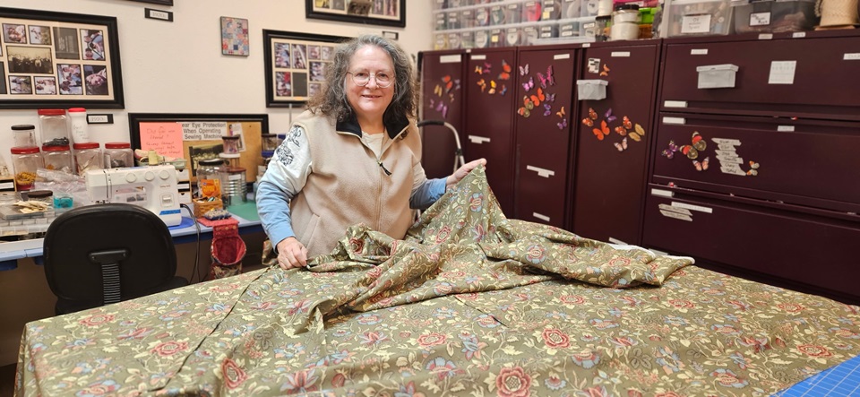 A woman holds up fabric inside the Fort Vancouver NHS Costume Shop.