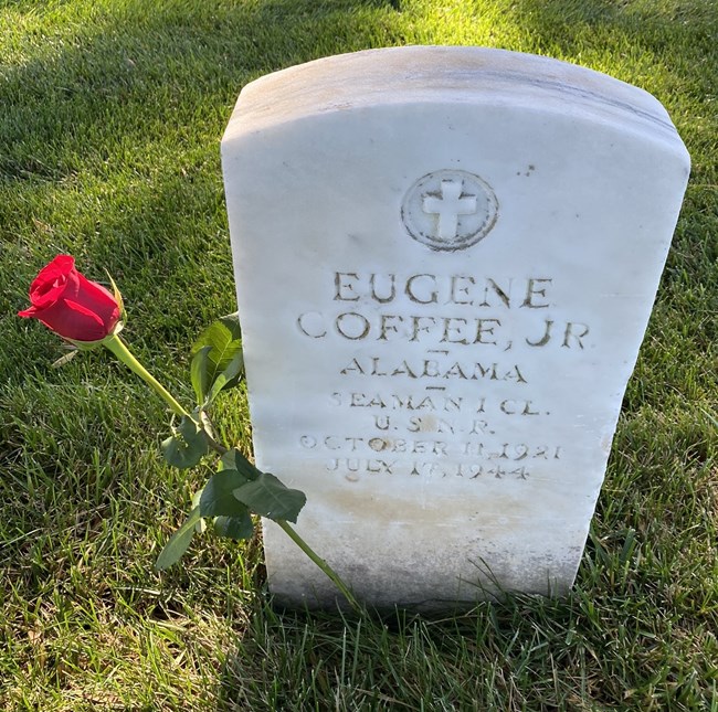 Gravestone engraved with cross, Eugene Coffee Jr, single rose placed to the left