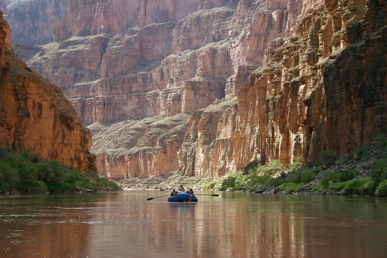 Photo of a raft floating on a river in a steep-sided canyon.