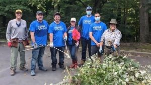 Ana Chuquin, shown in park uniform, stands behind a pile of removed invasive plant matter with a group of volunteers.