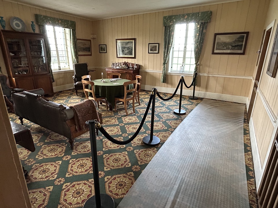The McLoughlin Sitting Room inside the Chief Factor's House. A Victorian-style parlor with polished wooden furniture, a sofa, a sideboard, table, and bookcase.