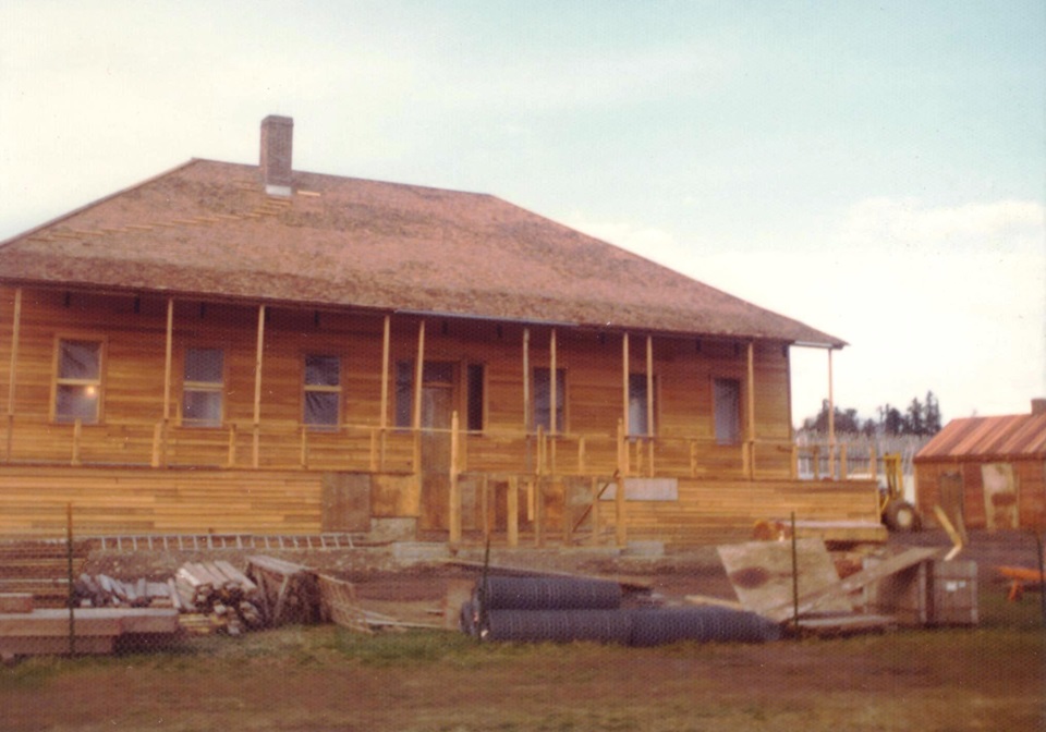 The Chief Factor's House under construction on a sunny day. The house is wooden and unpainted. Construction equipment and materials lie on the ground in front of the house.
