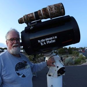 A man in a “Grand Canyon Star Party” shirt stands beside a large telescope.