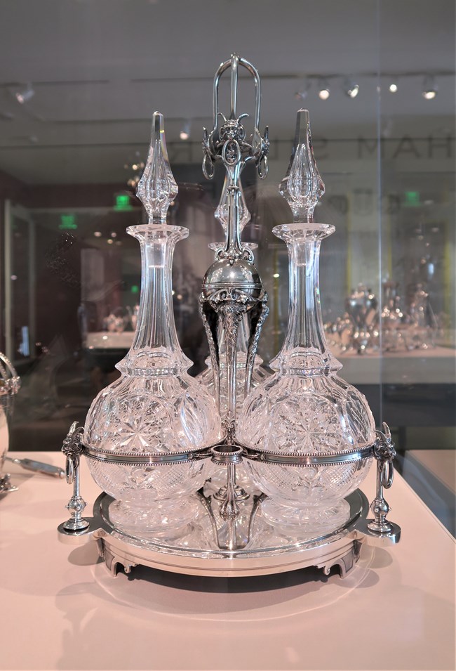 Three cut glass decanters with stoppers sitting in a silver holder.