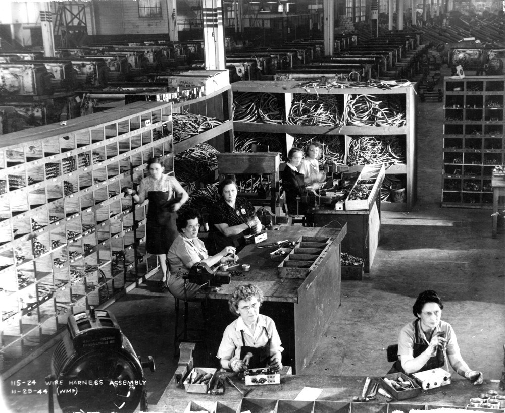 Black and white photo of a room filled with shelves and several women at workbenches