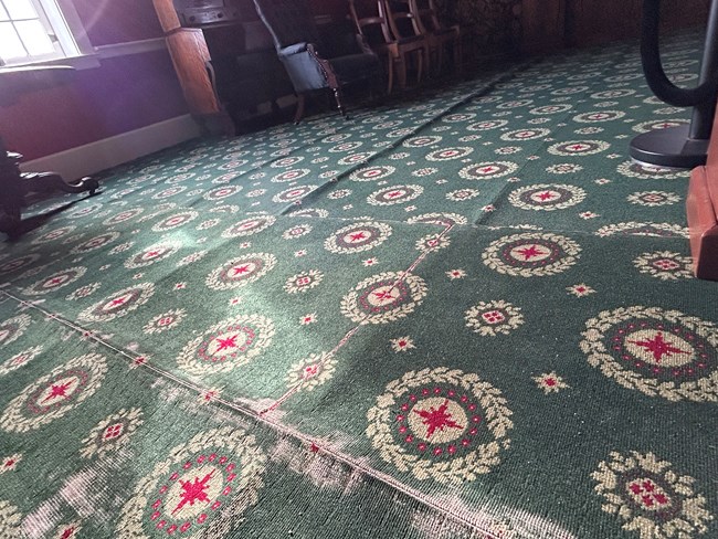 A close-up photo of the Douglas Sitting Room carpet in the Chief Factor's House. The carpet is threadbare and rippling due to water damage.