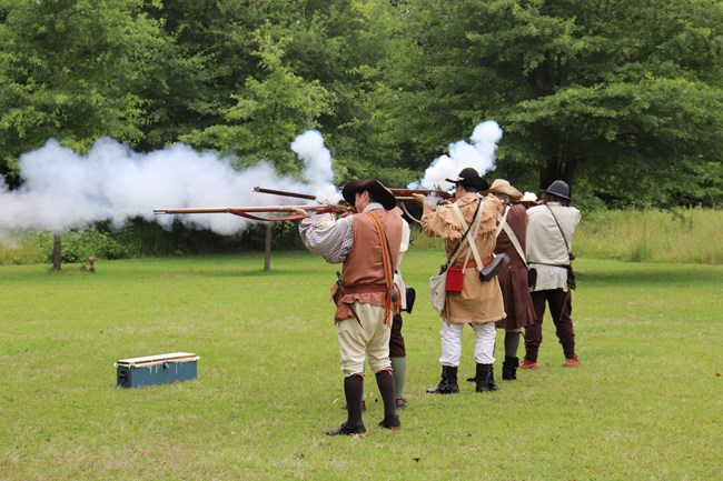 Several reenactors fire muskets.