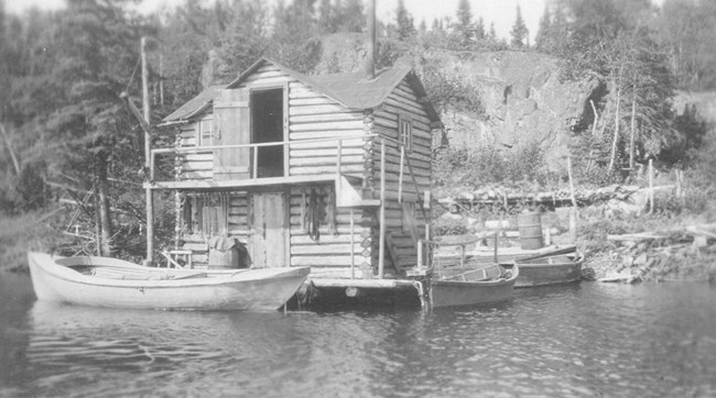 two story, log hewn fish house with dock surrounding it and two boats docked