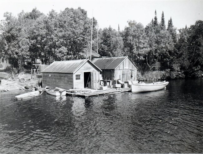 two fishhouses side by side with three boats in front and the left house's door open