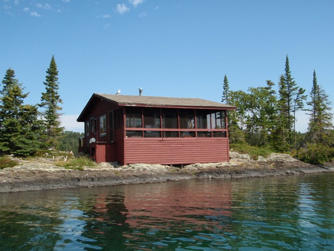 red cabin sitting very close to the edge of the waterway with screened in porch