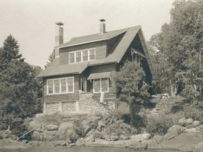 ornate two story house overlooking Rock Harbor channel, woman waving from front steps