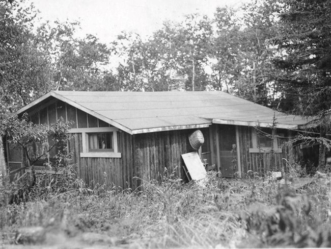 cabin with metal pail hanging near back door and table resting against structure