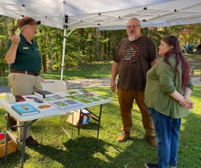 A woman in a Volunteer-in-Parks uniform speaks with two park visitors.