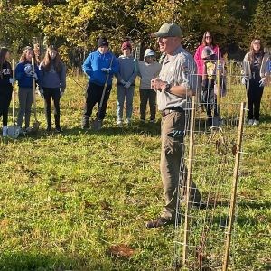 A man in a park ranger uniform stands in the middle of youth volunteers holding shovels.