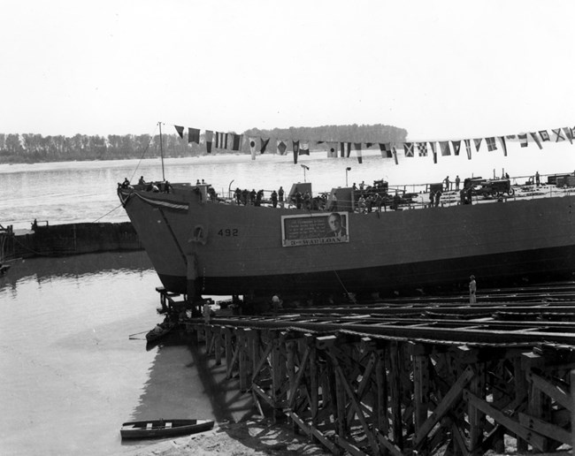 Black and white photo of ship with flags on a scaffolded platform on the water