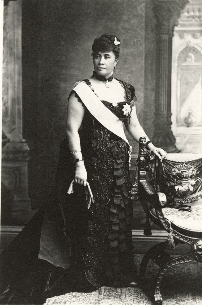 A woman standing next to a chair. She is wearing a sash.