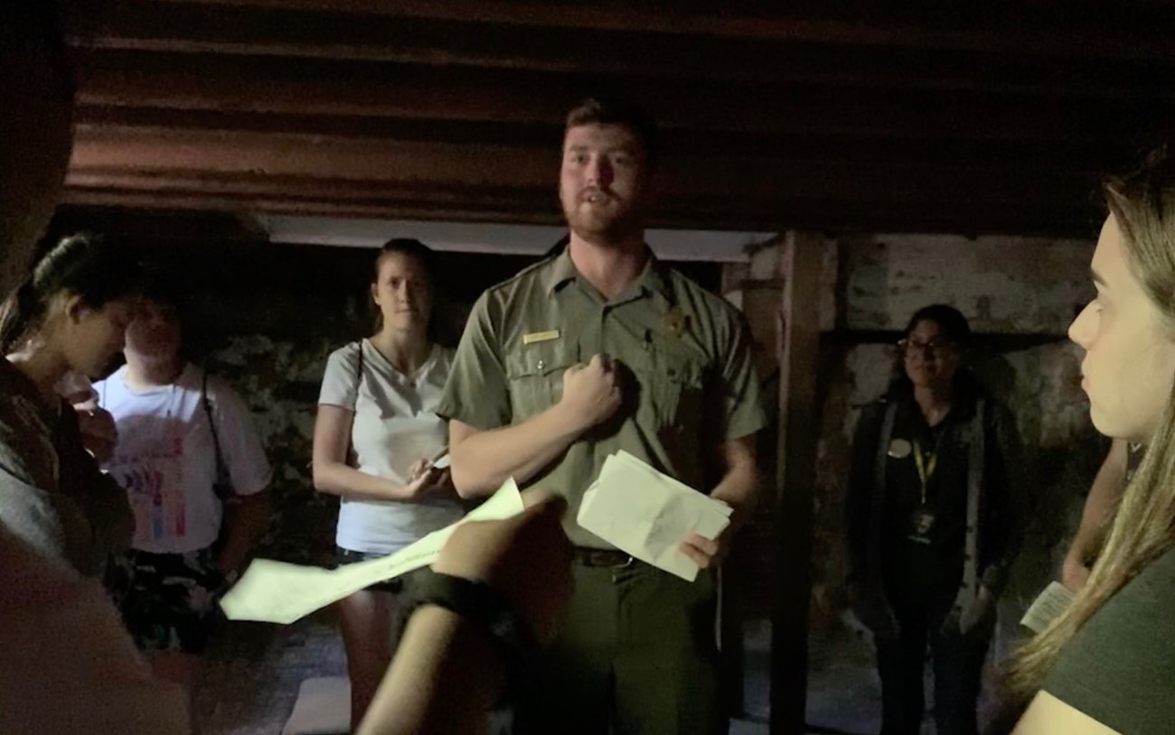 A park ranger talking to a group of people in a dark cellar
