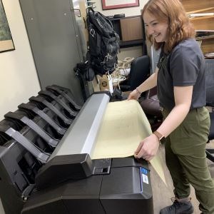 A young woman wearing a Volunteer-In-Parks uniform, scans a historic document into a large machine.