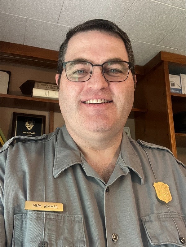 a person wearing glasses smiles at the camera, the name tag reads "Mike Wimmer"