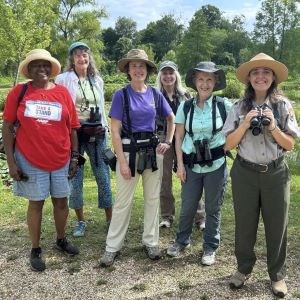 Molly Herman, wearing a purple shirt, is shown with a smiling group of birdwatchers, including a park ranger.