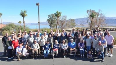 A group of volunteers stand and part staff in a parking lot with a lake and mountains in the background.