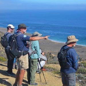 A volunteer giving an interpretative talk to visitors points to a large body of water.