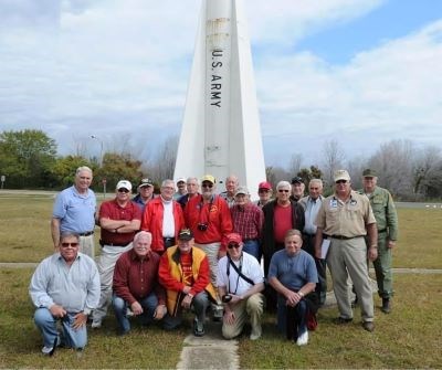 A group of male volunteers stand in front of a historic missile with park staff.