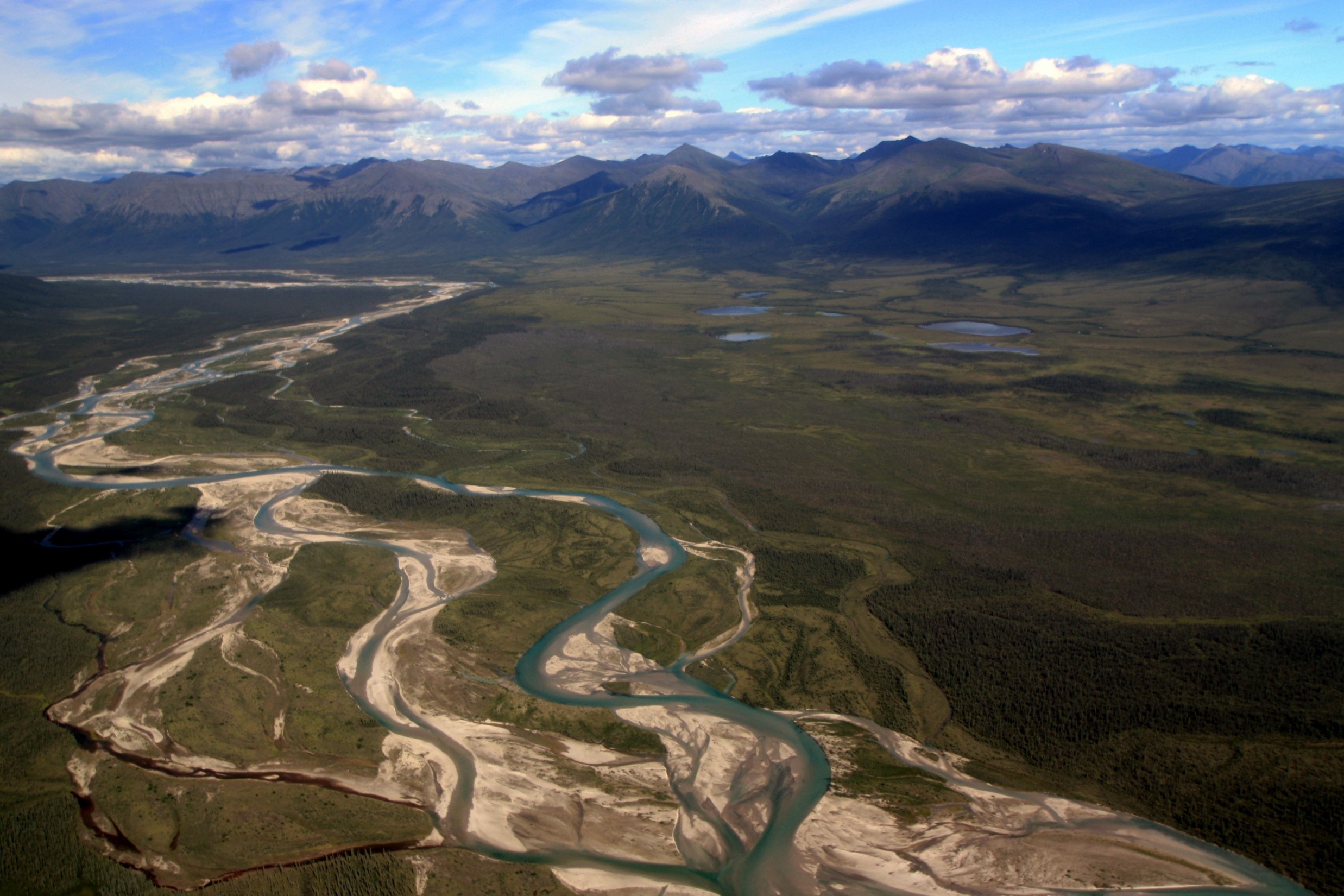 Aerial image of a Braided river in Alaska’s Arctic Network with mountains in background and a partly cloudy sky