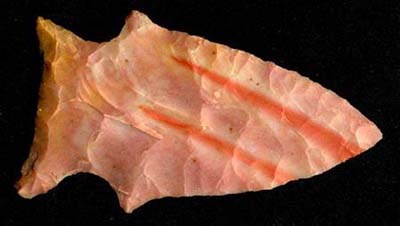 A flaked arrowhead in various shades of orange, yellow and cream color.