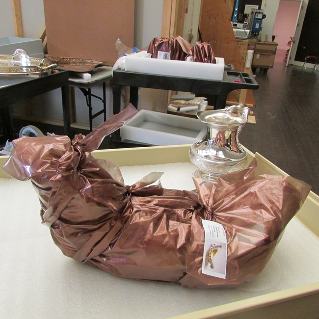 Cleaned silver objects on cart ready to return to storage. Some objects have been wrapped in anti-tarnish copper-impregnated sheeting while others are waiting to be wrapped.