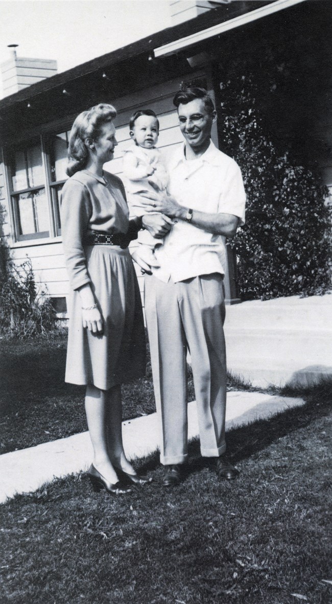 Black and white photo of young couple with baby in front of house