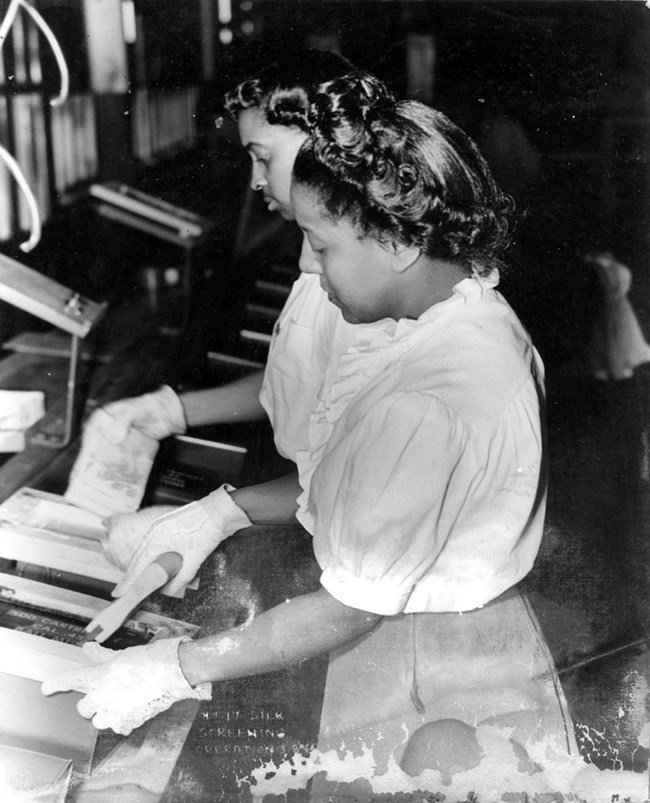 Black and white photo of two Black women in white gloves working along an assembly line.