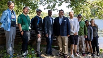 A group of volunteers pose in a park with the Director of the National Park Service.