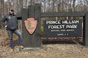 A man stands by a park entrance sign.