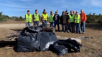 A group of volunteers wearing safety vests stand behind trash bags full of debris.