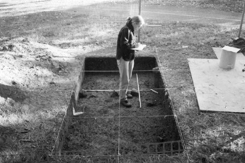 A person stands in an excavated archeological unit