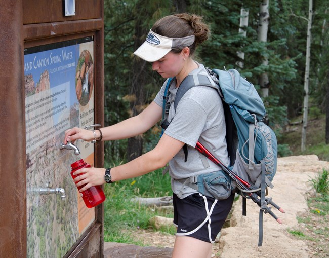 a woman with hiking pack fills a water bottle at an outdoor water bottle filling station