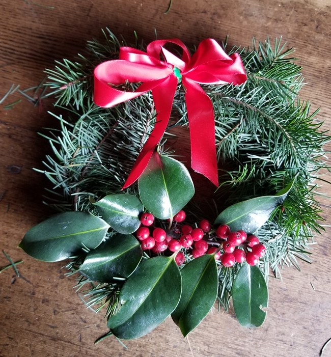 A wreath made with evergreen branches and a red ribbon.