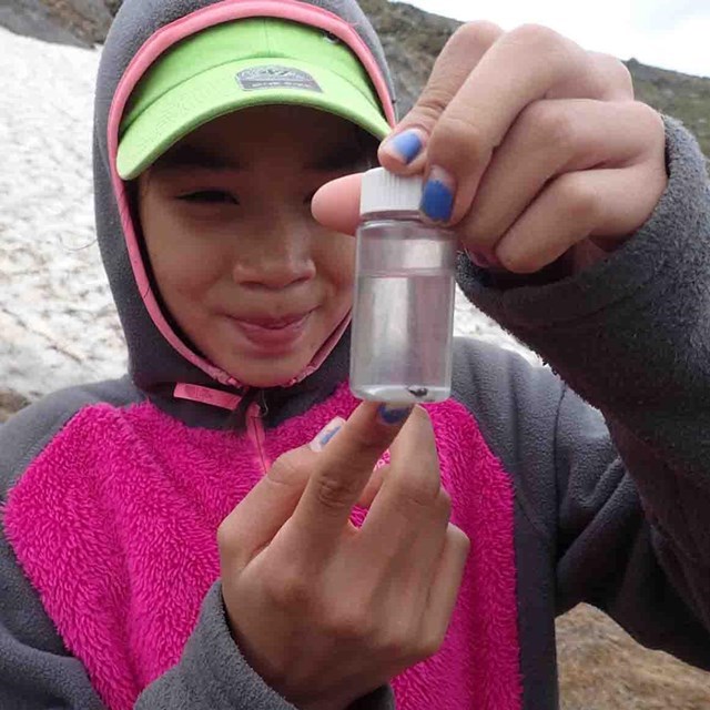 A young girl looks at a water sample in a jar.