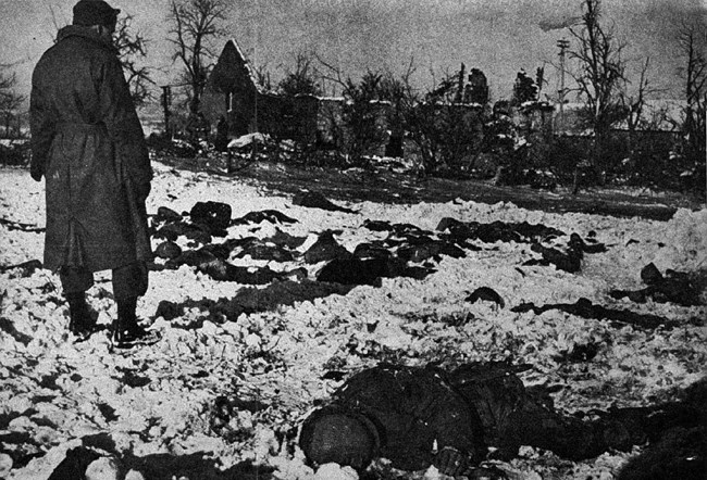 A black and white image showing a soldier looking over the bodies of fallen soldiers in the snow