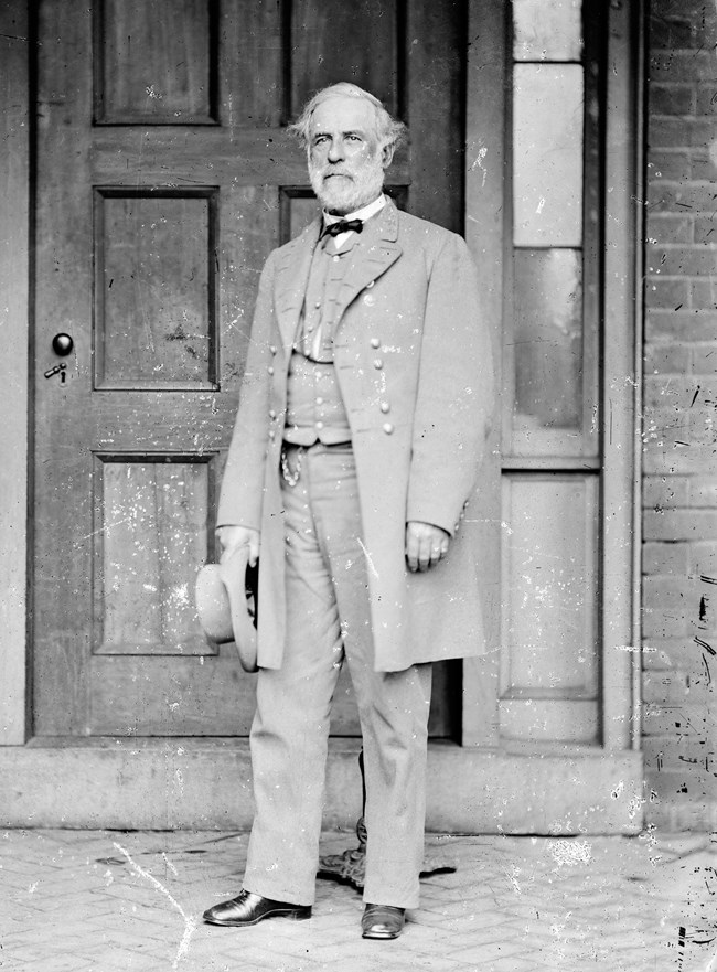 Black and white photo of man during Civil War wearing a gray suit, standing in front of a door.