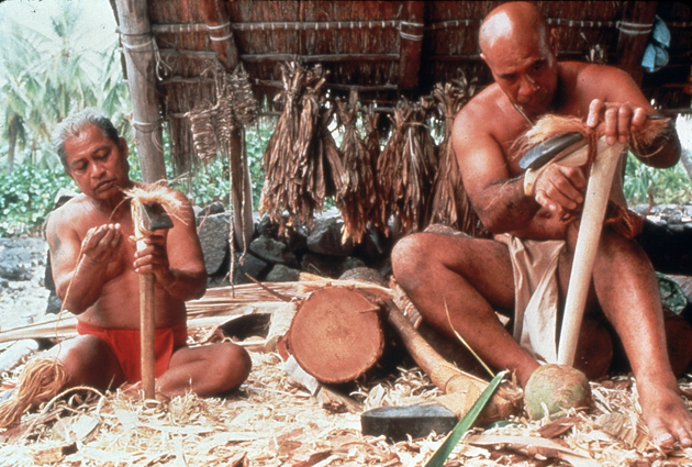 Two men in traditional clothing prepare ko'i (stone adz).