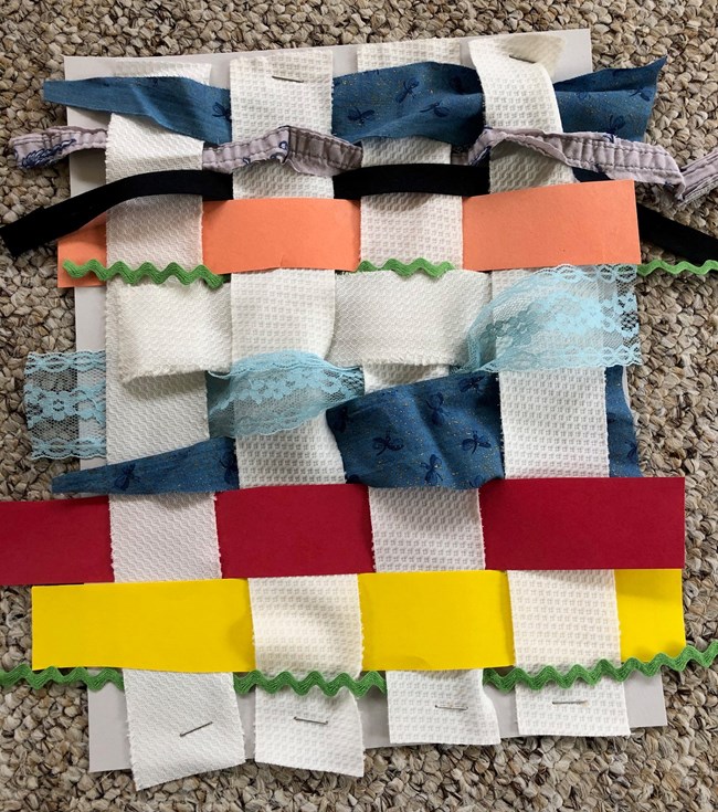 A complete simple weaving made from strips of colorful construction paper and fabric scraps.