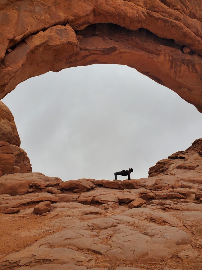 Inside a large orange colored natural sock arch, is poised a person in a back bend position.