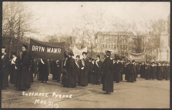 Postcard image of women in caps and gowns in street. Banners read "Bryn Mawr" and "Wellesley."
