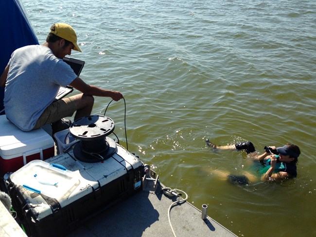a person floats in the water with camera equipment while a person deploys rope off a boat