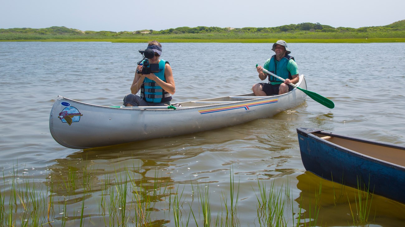 two people sit in a canoe in a marsh with cameras
