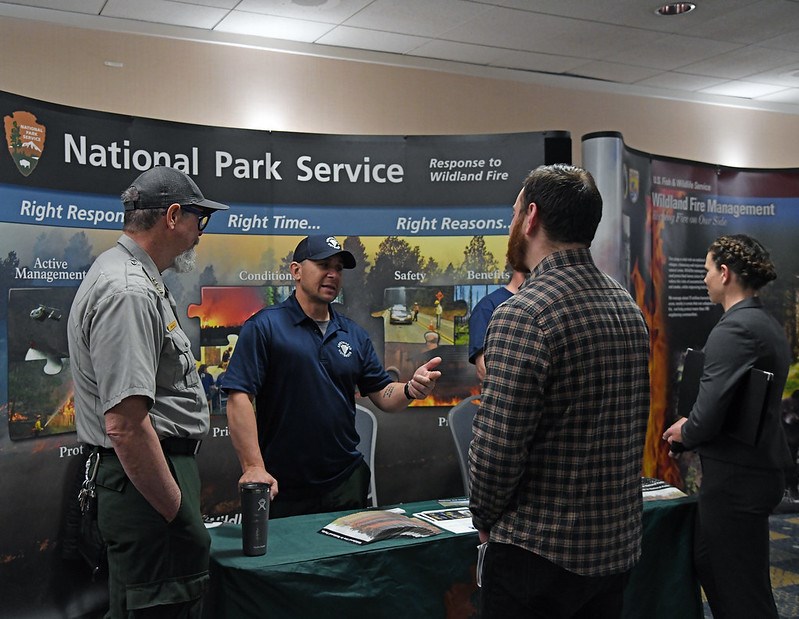 National Park Service employees meet with job candidates in front of a display about the wildland fire program.